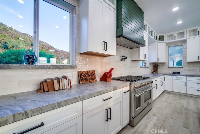 kitchen featuring range with two ovens, light hardwood / wood-style floors, white cabinetry, and premium range hood