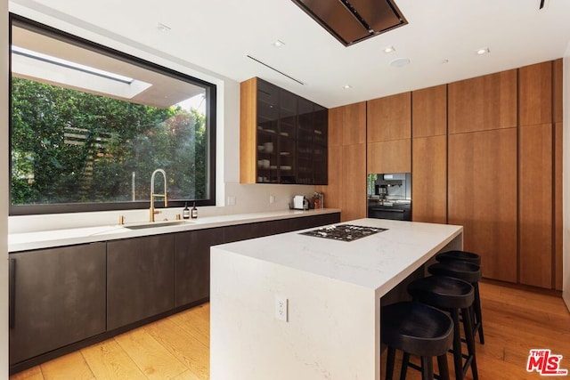 kitchen featuring a kitchen bar, sink, a center island, light hardwood / wood-style flooring, and gas cooktop