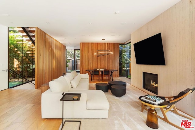 living room featuring plenty of natural light, a large fireplace, an inviting chandelier, and wood walls