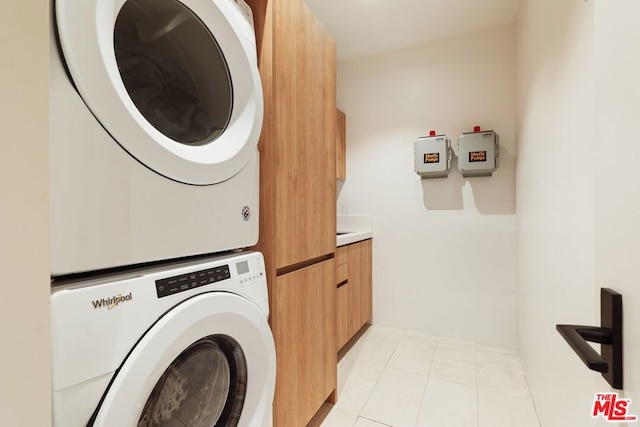 washroom with light tile patterned floors, cabinets, and stacked washing maching and dryer