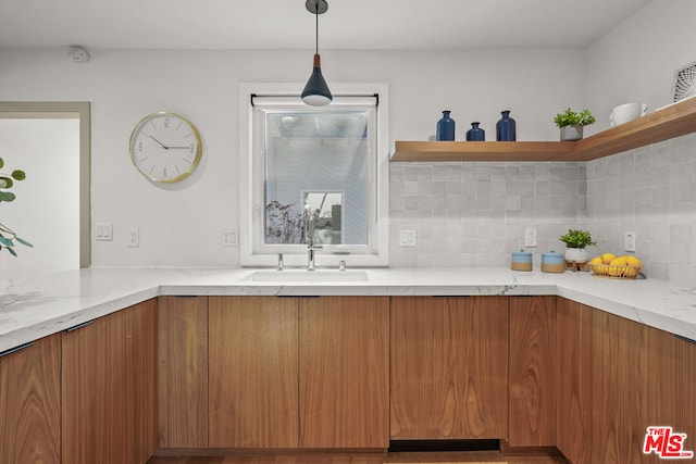 kitchen featuring backsplash, light stone counters, hanging light fixtures, and sink