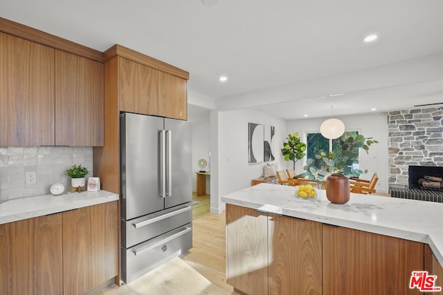 kitchen featuring light stone countertops, backsplash, light hardwood / wood-style flooring, and high quality fridge