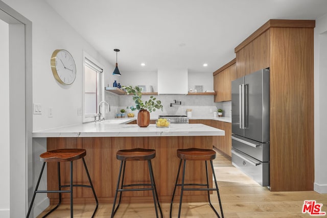 kitchen with kitchen peninsula, appliances with stainless steel finishes, decorative backsplash, sink, and light hardwood / wood-style flooring