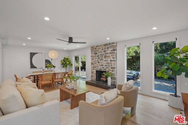 living room with light wood-type flooring, a stone fireplace, and ceiling fan