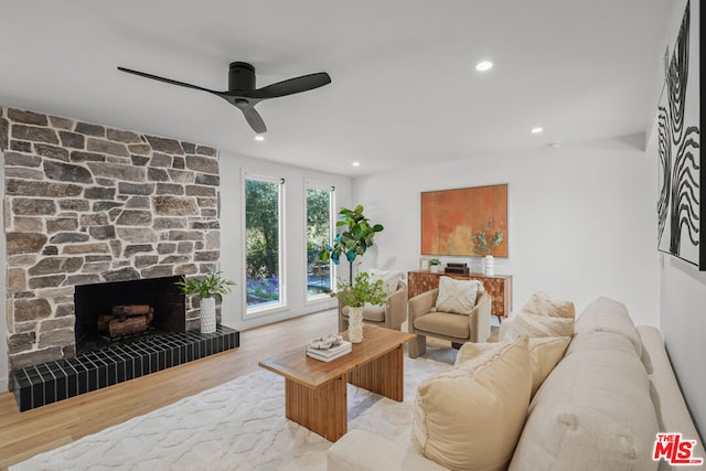 living room featuring a stone fireplace, ceiling fan, and light wood-type flooring