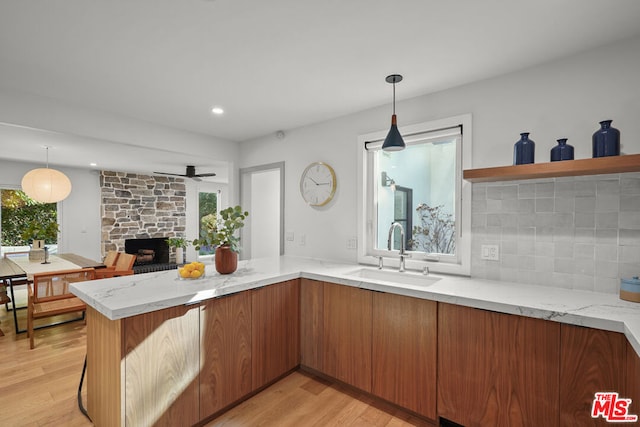 kitchen with light stone countertops, sink, hanging light fixtures, and light hardwood / wood-style flooring