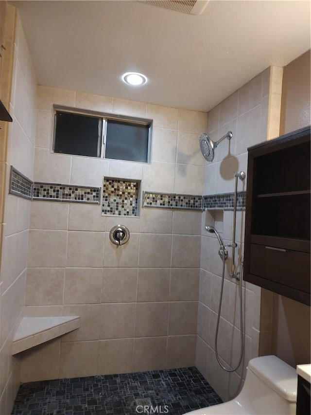 bathroom featuring a tile shower, vanity, and toilet