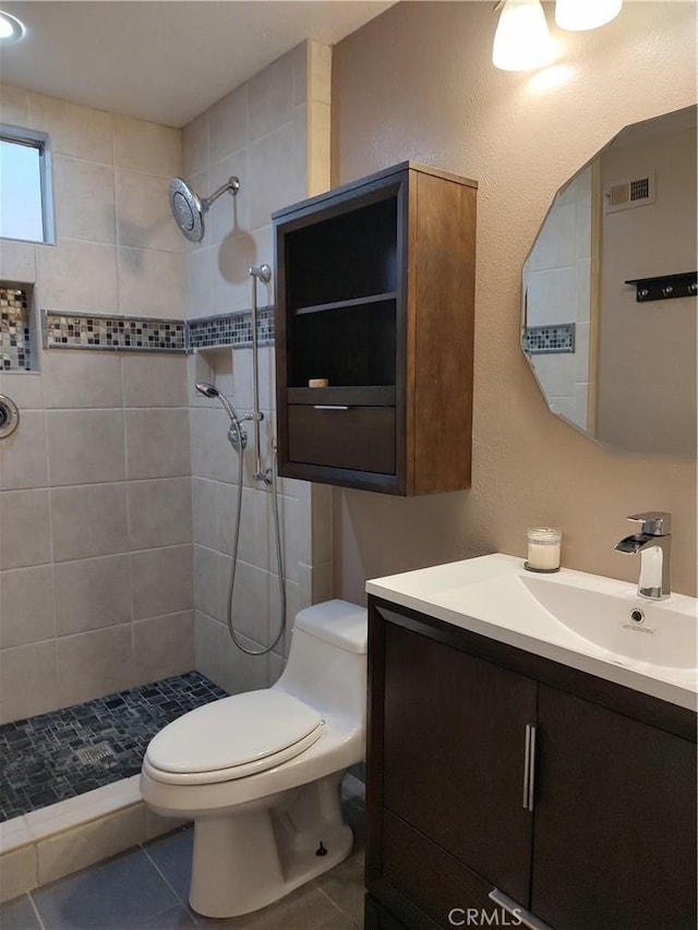 bathroom with tile patterned flooring, a tile shower, vanity, and toilet