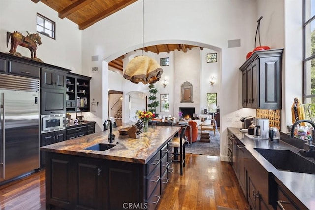 kitchen with wooden ceiling, high vaulted ceiling, a center island with sink, sink, and built in appliances