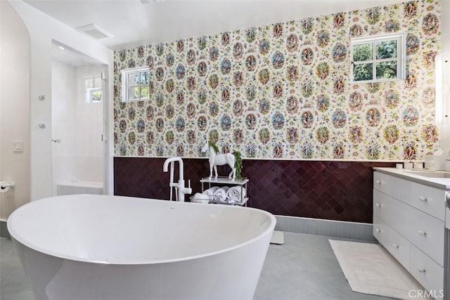 bathroom with vanity, a bathtub, tile walls, and a wealth of natural light