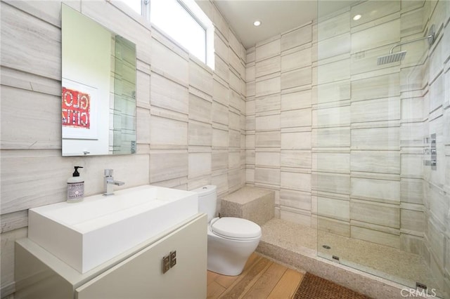 full bath with tile walls, toilet, vanity, wood finished floors, and tiled shower