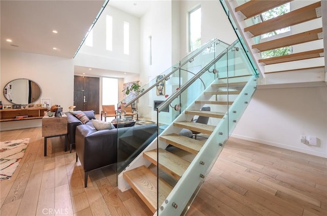 staircase with a towering ceiling, hardwood / wood-style flooring, baseboards, and recessed lighting