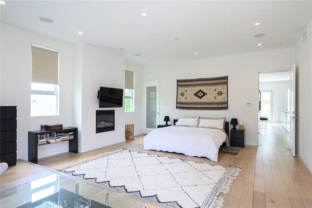 bedroom featuring light wood-type flooring, a glass covered fireplace, baseboards, and recessed lighting