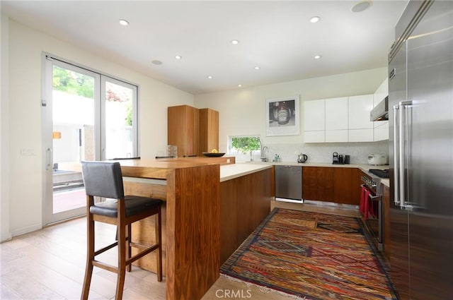 kitchen featuring premium appliances, tasteful backsplash, white cabinetry, modern cabinets, and a kitchen breakfast bar