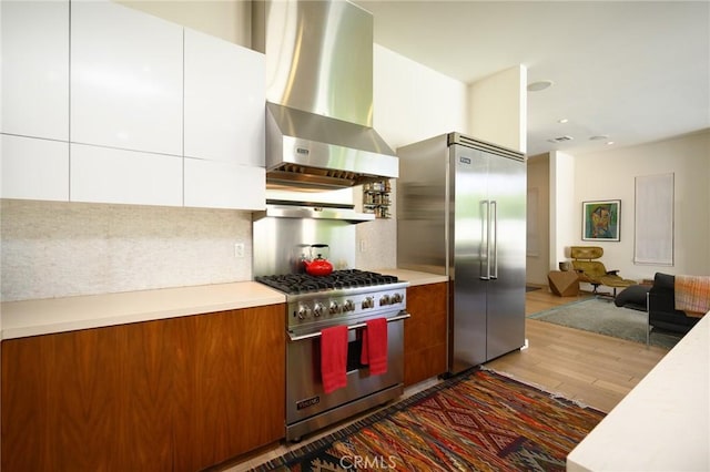 kitchen featuring premium appliances, range hood, light countertops, and wood finished floors