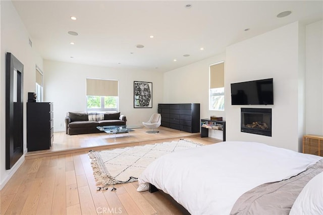 bedroom with light wood finished floors, a glass covered fireplace, visible vents, and recessed lighting