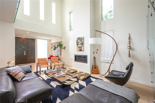 living room featuring a glass covered fireplace, a healthy amount of sunlight, baseboards, and wood finished floors