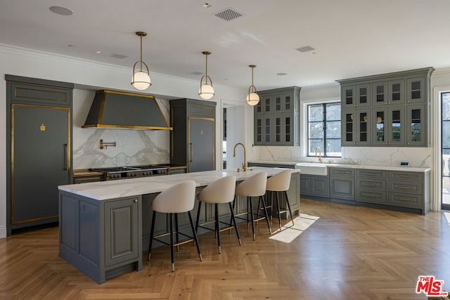 kitchen with paneled fridge, custom range hood, gray cabinetry, and a kitchen island with sink