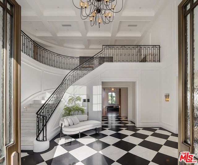 foyer with coffered ceiling, an inviting chandelier, ornamental molding, beamed ceiling, and a towering ceiling