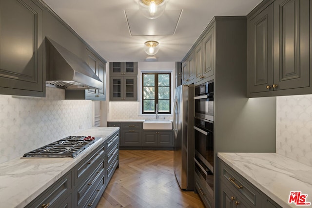 kitchen featuring wall chimney exhaust hood, stainless steel appliances, sink, and light stone counters