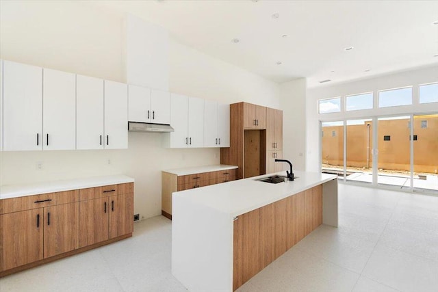 kitchen featuring sink, white cabinetry, a kitchen island with sink, and a high ceiling