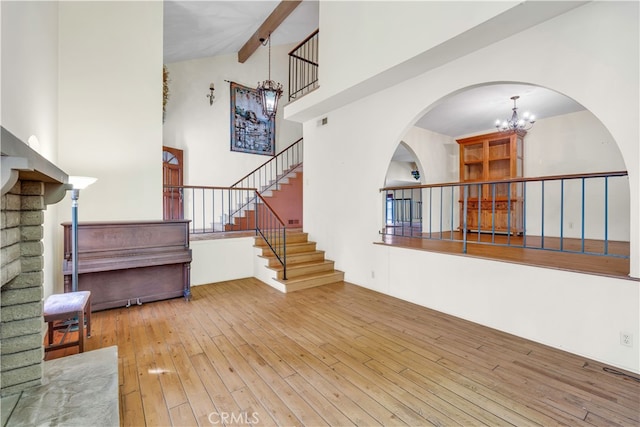 interior space with an inviting chandelier, beam ceiling, light hardwood / wood-style flooring, and high vaulted ceiling