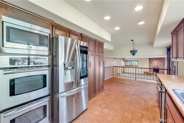 kitchen featuring sink, decorative light fixtures, a brick fireplace, appliances with stainless steel finishes, and tile counters