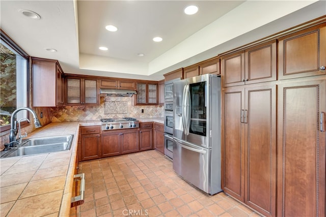 kitchen featuring sink, stainless steel appliances, decorative backsplash, tile countertops, and a raised ceiling