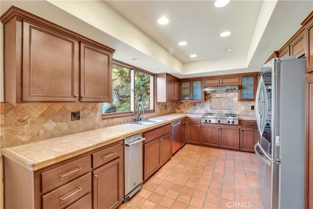 kitchen with sink, tile countertops, a raised ceiling, stainless steel appliances, and decorative backsplash