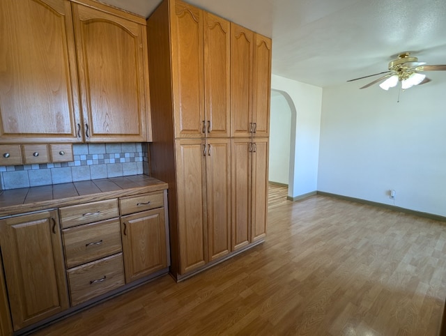 kitchen with tile countertops, light hardwood / wood-style flooring, backsplash, and ceiling fan