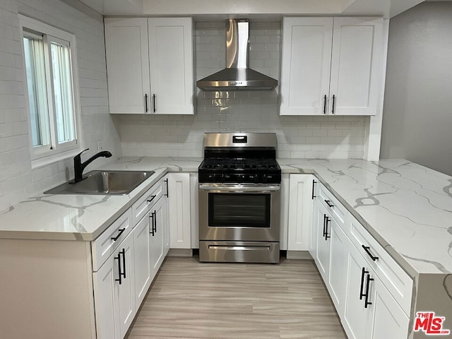 kitchen with stainless steel gas range oven, wall chimney exhaust hood, white cabinets, light stone counters, and sink