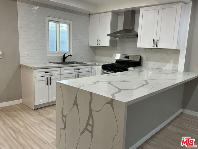 kitchen featuring light stone countertops, white cabinetry, wall chimney range hood, sink, and stainless steel range with gas stovetop