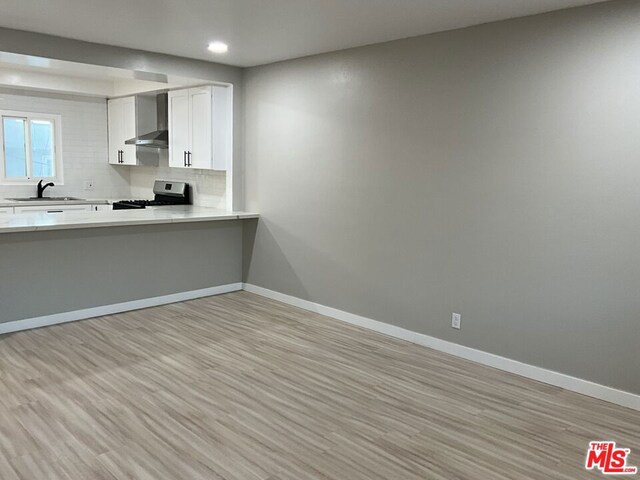 kitchen featuring white cabinets, wall chimney exhaust hood, stainless steel range, backsplash, and light hardwood / wood-style flooring