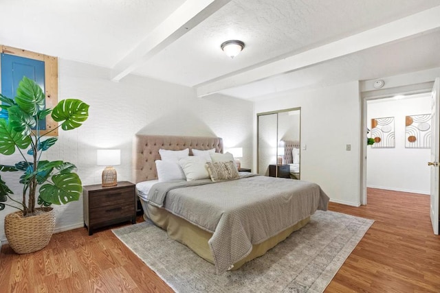 bedroom with beamed ceiling, a closet, light hardwood / wood-style flooring, and a textured ceiling