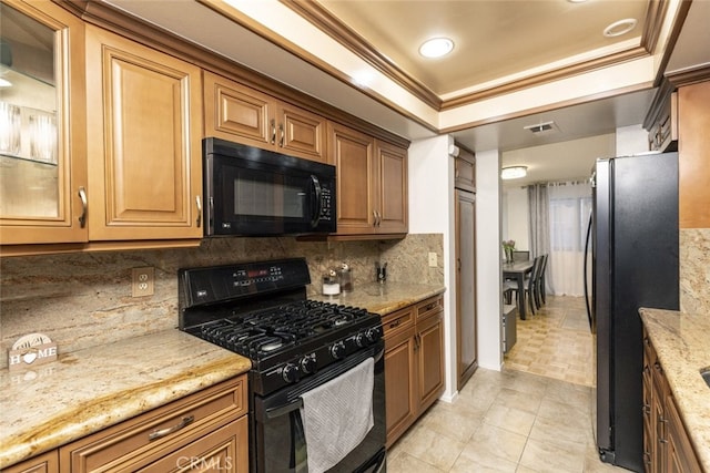 kitchen with decorative backsplash, light stone counters, a tray ceiling, and black appliances