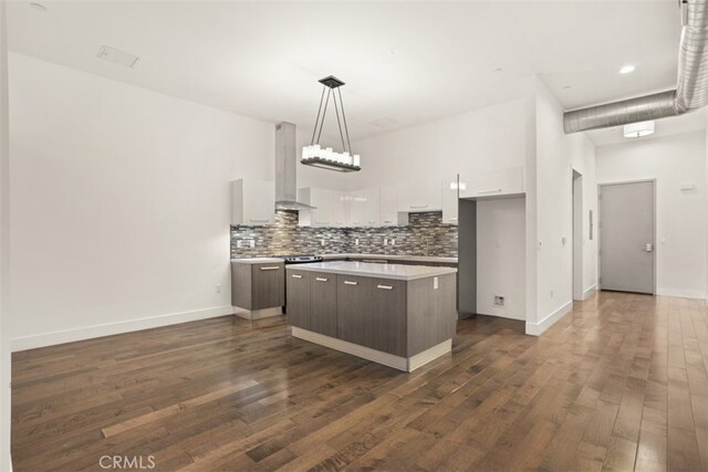 kitchen featuring wall chimney range hood, a kitchen island, dark hardwood / wood-style flooring, white cabinetry, and dark brown cabinetry