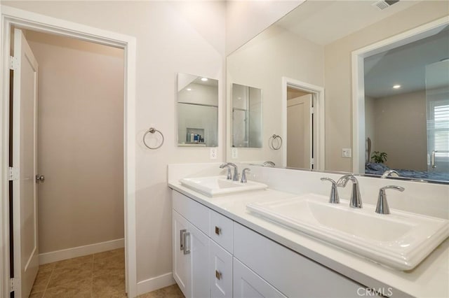 ensuite bathroom featuring double vanity, a sink, baseboards, and tile patterned floors