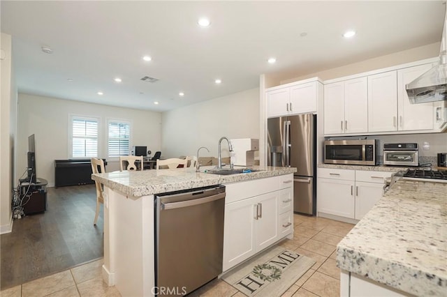 kitchen featuring a breakfast bar, stainless steel appliances, white cabinetry, a sink, and an island with sink