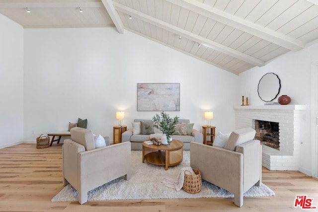 living room with vaulted ceiling with beams, light wood-type flooring, and a fireplace