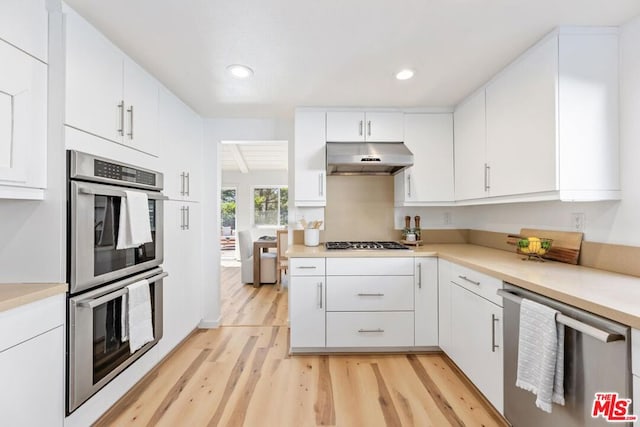 kitchen featuring exhaust hood, white cabinetry, stainless steel appliances, and light wood-type flooring