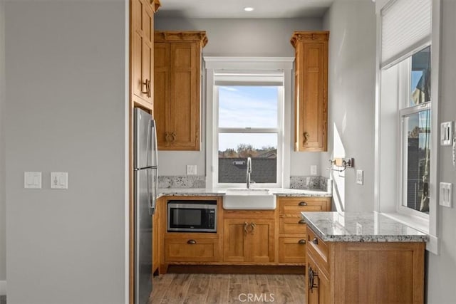 kitchen featuring light hardwood / wood-style flooring, light stone countertops, sink, and stainless steel appliances