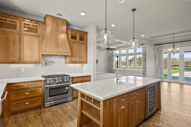 kitchen with sink, an island with sink, decorative light fixtures, light hardwood / wood-style floors, and stainless steel appliances