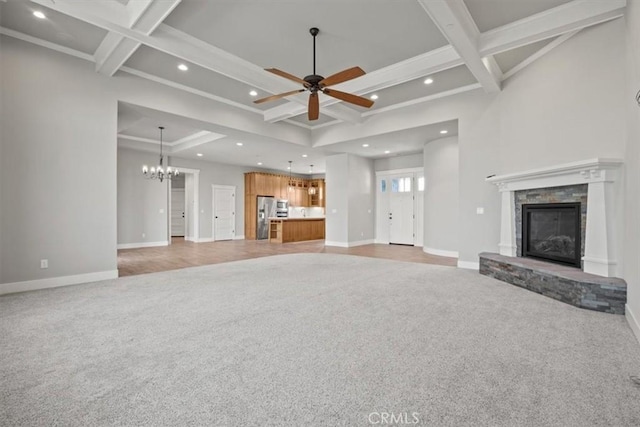 unfurnished living room with coffered ceiling, ceiling fan with notable chandelier, light colored carpet, beam ceiling, and a stone fireplace