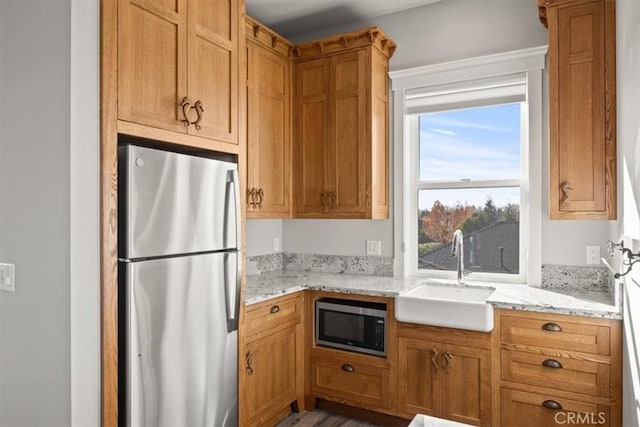 kitchen featuring hardwood / wood-style floors, stainless steel appliances, light stone counters, and sink