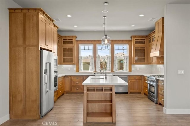 kitchen with a center island with sink, decorative light fixtures, light wood-type flooring, and appliances with stainless steel finishes