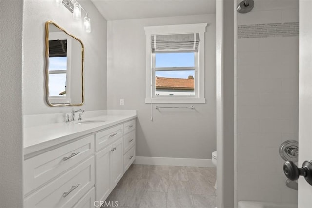 bathroom with a tile shower, vanity, and toilet