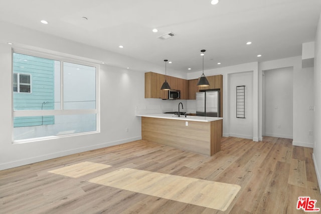 kitchen with kitchen peninsula, appliances with stainless steel finishes, sink, decorative light fixtures, and light hardwood / wood-style flooring