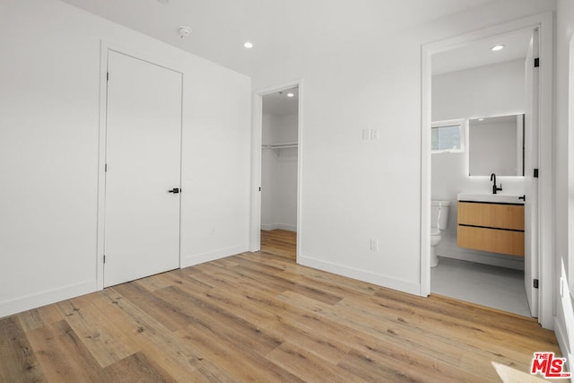 unfurnished bedroom featuring ensuite bathroom, light hardwood / wood-style flooring, a spacious closet, and sink