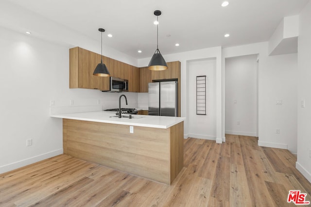 kitchen featuring kitchen peninsula, appliances with stainless steel finishes, sink, pendant lighting, and light hardwood / wood-style flooring