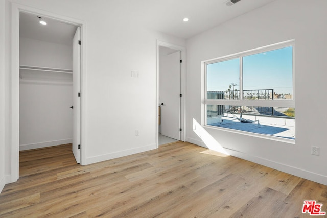 unfurnished bedroom with a walk in closet, a closet, and light hardwood / wood-style flooring